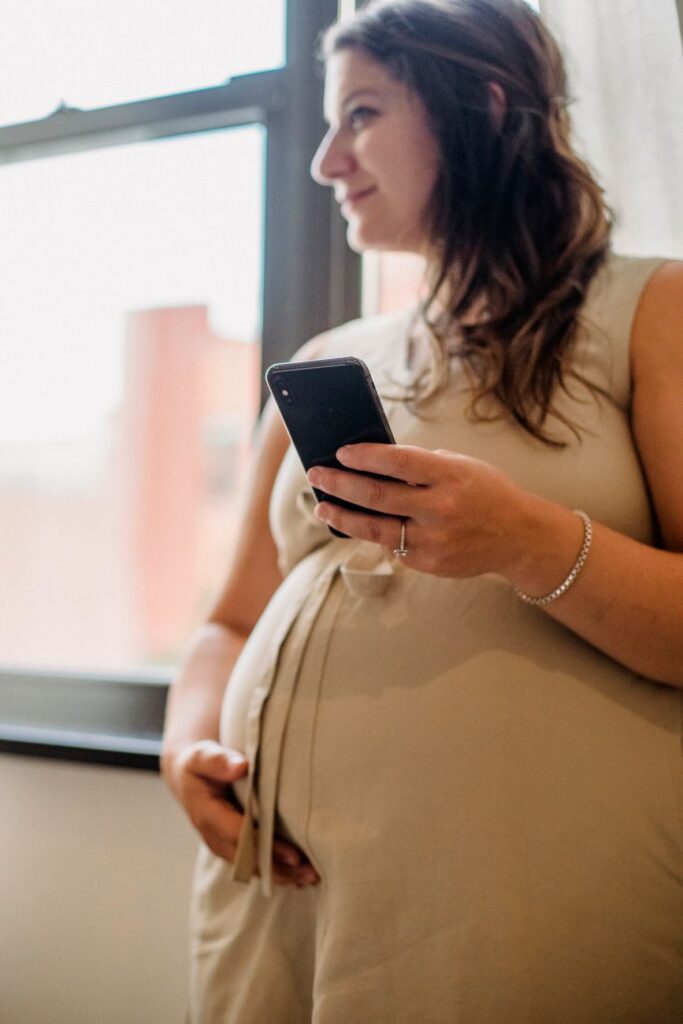 pregnant female using cellphone while standing in room